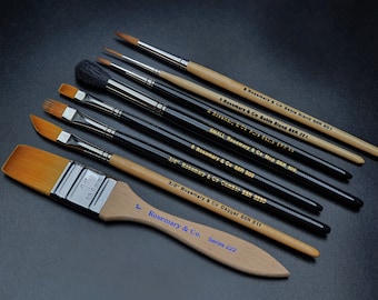 May include: A set of 8 Rosemary & Co. paint brushes, including a 1-inch flat brush, a 3/8-inch dagger brush, a 3/8-inch comb brush, a small mop brush, a sable blend brush, and three round brushes. The brushes are arranged in a row on a black surface.