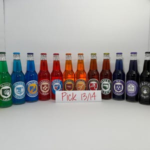 May include: A collection of glass soda bottles with colorful liquids and labels. The bottles are arranged in a row, each with a different color and design. The labels feature various graphics and text.