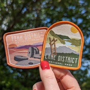 K&ouml;nnte beinhalten: Zwei gestickte Aufn&auml;her, einer mit dem Text "Peak District National Park" und einer Landschaftsszene, der andere mit dem Text "Lake District National Park" und einer Bergszene.