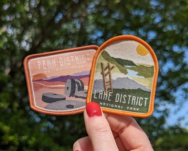 K&ouml;nnte beinhalten: Zwei gestickte Aufn&auml;her, einer mit dem Text "Peak District National Park" und einer Landschaftsszene, der andere mit dem Text "Lake District National Park" und einer Bergszene.