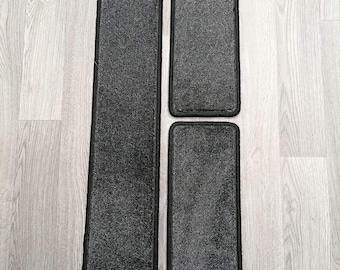 May include: A set of three dark gray carpeted floor mats with black fabric edging. The set includes one long, narrow mat with an angled top edge and two shorter, rectangular mats. Each piece features a textured, low-pile surface finish.