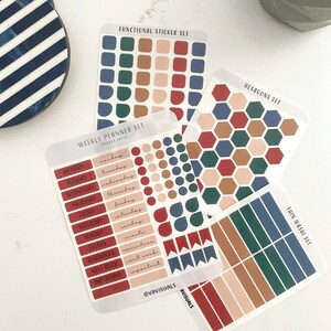 Op de afbeelding: Een verzameling plannerstickers in diverse vormen en kleuren. De stickers bevatten vierkanten, zeshoeken en banners in tinten rood, blauw, groen en beige. De tekst op de stickers luidt "Weekly Planner Set" en "Functional Sticker Set".