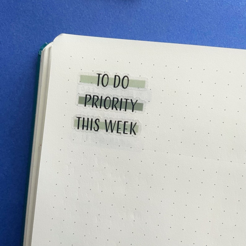 Op de afbeelding: Een witte pagina met drie groene en witte gestreepte labels met de tekst "TO DO", "PRIORITY" en "THIS WEEK" in zwart.