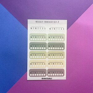 May include: A sheet of weekly tracker stickers with the text "WEEKLY TRACKER SET 2" at the top. The stickers are in various colors, including white, beige, light green, and gray. Each sticker has the days of the week labeled "MTWTFSS" and a row of seven circles for tracking.