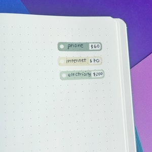 May include: A white page with three green and beige rectangular stickers with handwritten text. The stickers list phone, internet, and electricity with their corresponding prices. The prices are $60, $70, and $200.