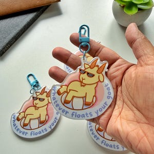 May include: Clear acrylic keyrings with a cartoon goat wearing sunglasses, and the text "whatever floats your goat" in light blue. Each keyring has a light blue clasp.