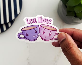Puede incluir: Una pegatina con dos tazas de té de dibujos animados con caras, una con una bolsita de té, y el texto "tea time" en letras rosas.