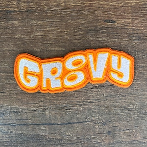 May include: Orange and white embroidered patch with the word "groovy" in white letters.