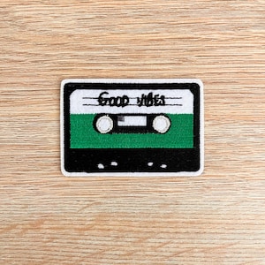 May include: An embroidered patch shaped like a cassette tape with the words "Good Vibes" on the top and a green cassette tape inside.