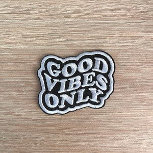 May include: A black and white embroidered patch with the text "GOOD VIBES ONLY" in a stylized font.