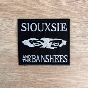 Könnte beinhalten: Schwarz-weiß gestickter Patch mit dem Text "Siouxsie and the Banshees" und einem stilisierten Bild von zwei Augen.