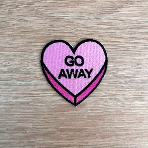 May include: Pink heart-shaped patch with black embroidery that reads "GO AWAY".