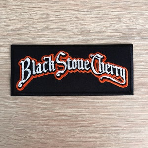 Peut inclure: Patch brodé Black Stone Cherry avec des lettres blanches soulignées d'orange sur fond noir.