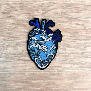 Könnte beinhalten: Blau-weißer gestickter Herz-Patch mit Wellenmuster.
