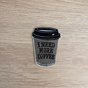 May include: An embroidered patch of a coffee cup in brown and black with the text "I NEED MORE COFFEE".