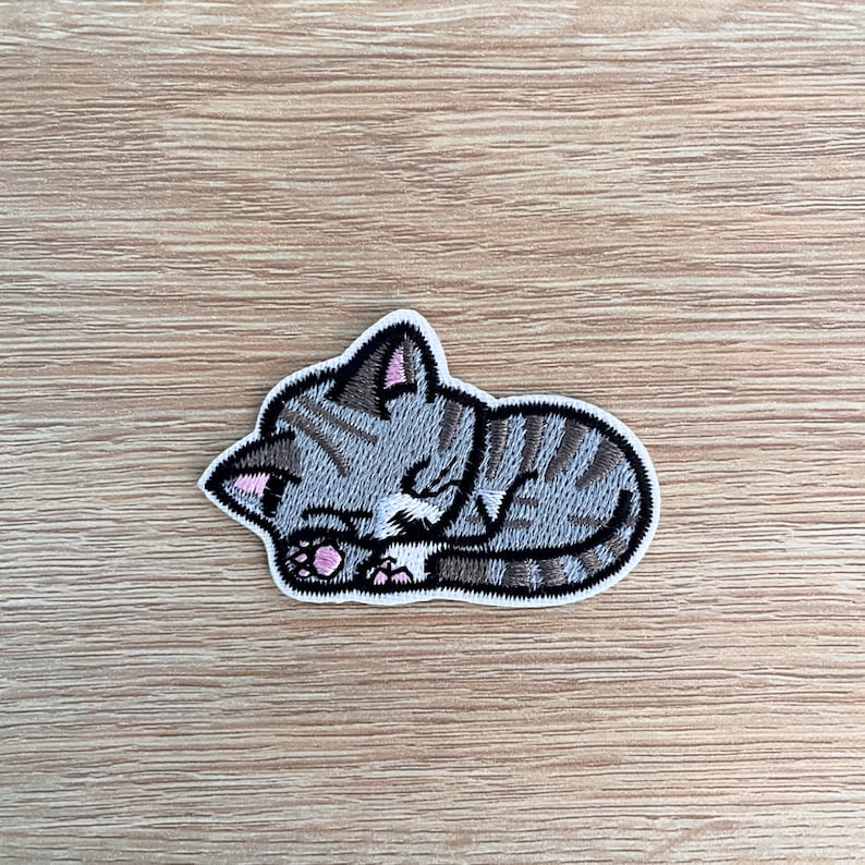 a sew or iron on embroidered patch of a cute grey coloured kitten asleep