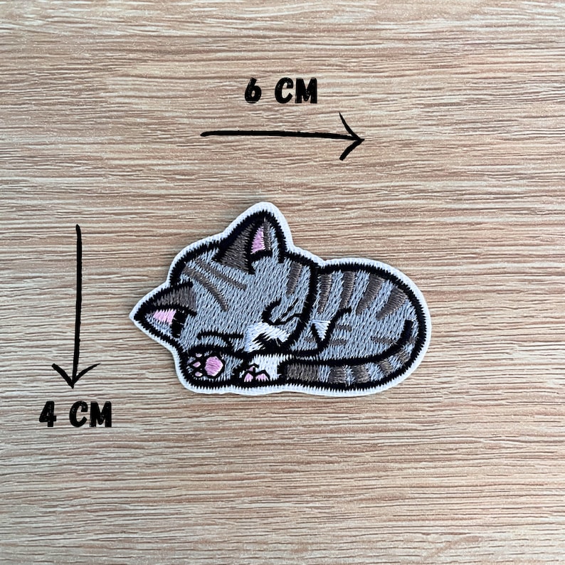 a sew or iron on embroidered patch of a cute grey coloured kitten asleep