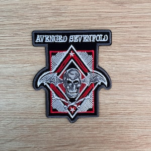 May include: A black and white embroidered patch with the band name "Avenged Sevenfold" in white text. The patch features a skull with wings and a red and white diamond shape.