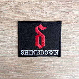 Könnte beinhalten: Schwarzer gestickter Patch mit einem roten stilisierten Buchstaben "S" und dem Text "SHINEDOWN" in Weiß.