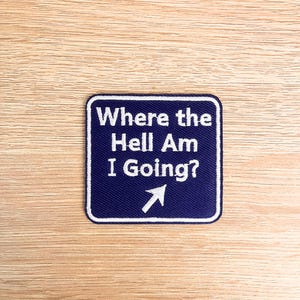 May include: A navy blue patch with white text reading "Where the Hell Am I Going?" and a white arrow pointing right. The patch has a white border. It is set against a light wood grain background.
