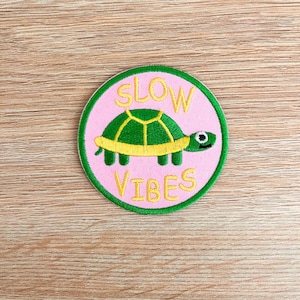 May include: An embroidered patch with a cartoon turtle and the text "SLOW VIBES" on a pink background with green stitching.