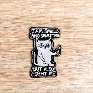 Könnte beinhalten: Schwarz-weiß gestickter Aufnäher mit einer Comic-Katze, die ein Messer hält. Der Text lautet "Ich bin klein und sensibel, aber auch kämpfe ich."