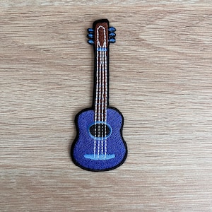 May include: A blue and brown embroidered patch of an acoustic guitar.