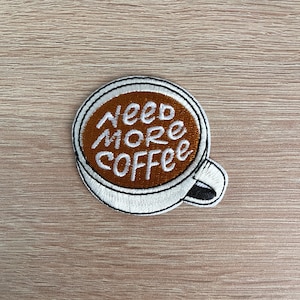 May include: White embroidered iron-on patch of a coffee cup with the text "Need More Coffee" in brown embroidery.