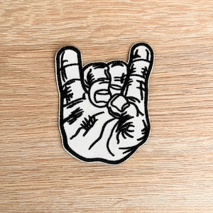 May include: Black and white embroidered patch of a hand making the rock and roll hand gesture.