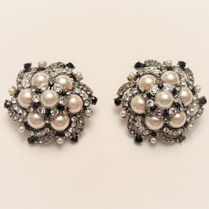 May include: A pair of silver tone earrings with a floral design. The earrings are adorned with white pearls and black rhinestones.