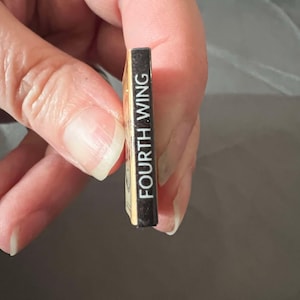 May include: A small, gold-colored book with a black spine that reads "FOURTH WING" in white text.