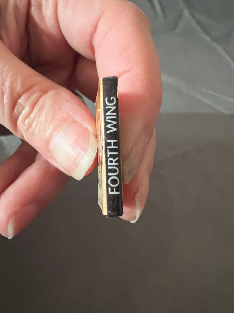 May include: A small, gold-colored book with a black spine that reads "FOURTH WING" in white text.