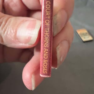 May include: A close-up of the spine of a book titled "A Court of Thorns and Roses". The spine is red with gold lettering.