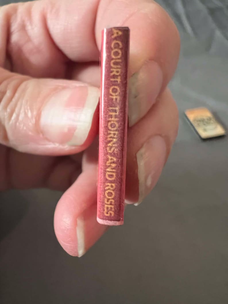 May include: A close-up of the spine of a book titled "A Court of Thorns and Roses". The spine is red with gold lettering.
