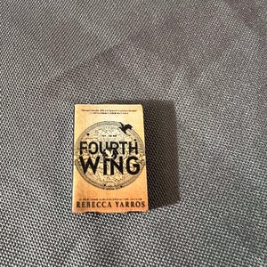 May include: A paperback book with a tan cover featuring a black and white illustration of a bird in a circle with the text "Fourth Wing" and the author's name "Rebecca Yarros".