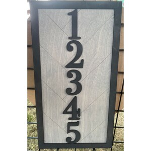 May include: A wooden sign with a black frame and a chevron pattern. The numbers 1, 2, 3, 4, and 5 are cut out of black wood and attached to the sign.