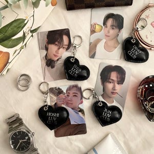 May include: Seven black heart-shaped keychains with silver rings. Each keychain has white text that reads "[Name] Luv Club" with the names being "Dino", "The8", "Hoshi", "Jun", "Wonwoo", "Mingyu", and "Seungkwan".