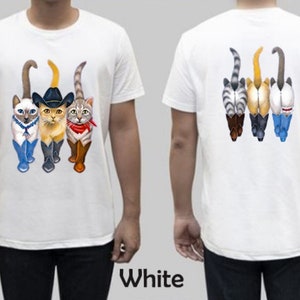 May include: White t-shirt with a graphic of four cats wearing boots and hats. The cats are walking in a line. The back of the shirt has a graphic of the cats' backsides.