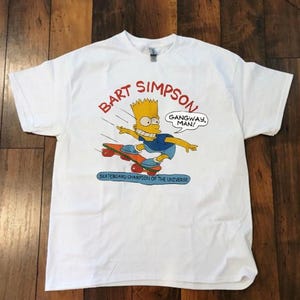 May include: White t-shirt with a cartoon image of Bart Simpson skateboarding. The design includes the text "BART SIMPSON" in red, a speech bubble saying "GANGWAY, MAN!", and "SKATEBOARD CHAMPION OF THE UNIVERSE" in blue.