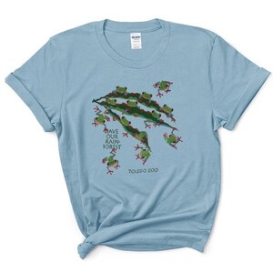 Op de afbeelding: Lichtblauw T-shirt met een afbeelding van groene boomkikkers op een tak. De tekst "Save Our Rainforest" en "Toledo Zoo" staan op het shirt gedrukt.