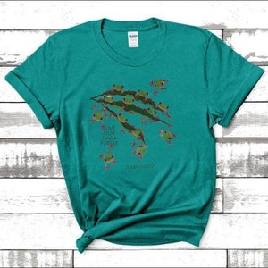 Op de afbeelding: Een turquoise t-shirt met een afbeelding van groene boomkikkers op een tak. De tekst "Save Our Rain Forest" is op het shirt gedrukt. Het shirt heeft een ronde hals en korte mouwen.
