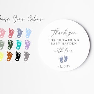 May include: A round white sticker with the text "Thank you for showering baby Hayden with love" and the date "02.10.25".  The sticker also features two small blue footprints with hearts.  A colour chart with 12 different coloured footprints is shown in the background.