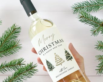 May include: A clear wine bottle with a dark green cap and a label that reads "Merry Christmas & A Happy New Year." The label features three illustrated Christmas trees. The bottle is held by a person.