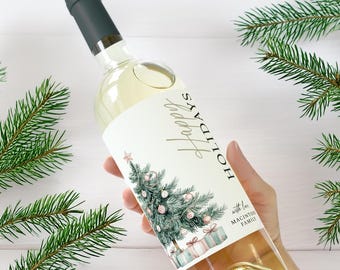 May include: A clear wine bottle with a dark green cap and a label that reads "Happy Holidays." The label features a watercolor Christmas tree with ornaments and gifts. The bottle is surrounded by evergreen branches.