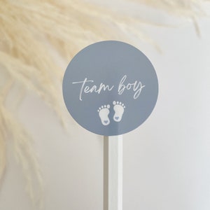 May include: A blue circle sticker with the text "Team Boy" in white script and two white footprints with a small pink heart in each footprint.