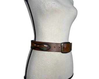May include: A brown leather belt with a decorative design featuring a snake with green, orange, and white accents. The belt has a brass buckle.