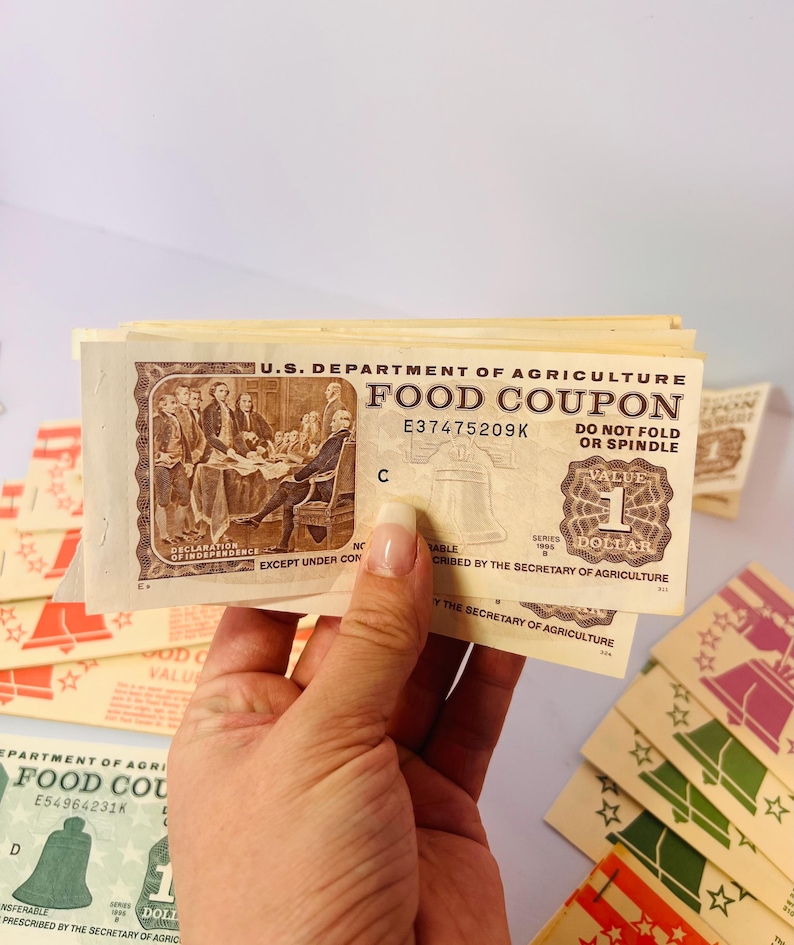 May include: A stack of vintage U.S. Department of Agriculture Food Coupons. The coupons are beige with brown ink, featuring illustrations of the Declaration of Independence and the Liberty Bell. Each coupon is worth one dollar.