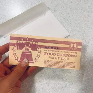 May include: A vintage U.S. Department of Agriculture food coupon with a value of $7.00. The coupon features a design with a bell and stars in a pink and beige color scheme. The text includes the coupon's serial number and an equal opportunity statement.