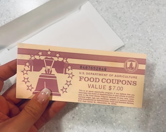 May include: A vintage U.S. Department of Agriculture food coupon with a value of $7.00. The coupon features a design with a bell and stars in a pink and beige color scheme. The text includes the coupon's serial number and an equal opportunity statement.