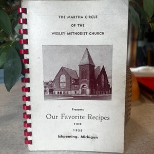 May include: A vintage cookbook titled "Our Favorite Recipes" for the Martha Circle of the Wesley Methodist Church in Ishpeming, Michigan, 1958. The cover features a black and white photo of the church.